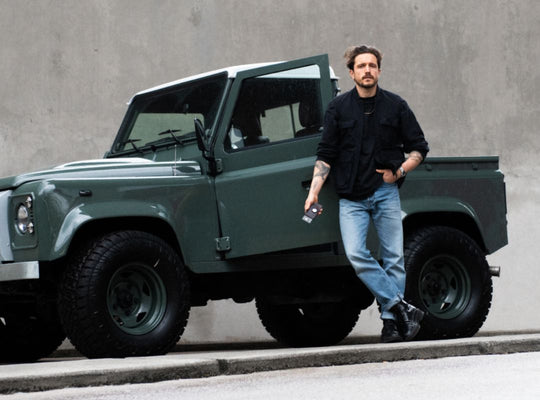 Rugged man holding Ekter's aluminum cardholder leaning against a Land Rover Defender car. 